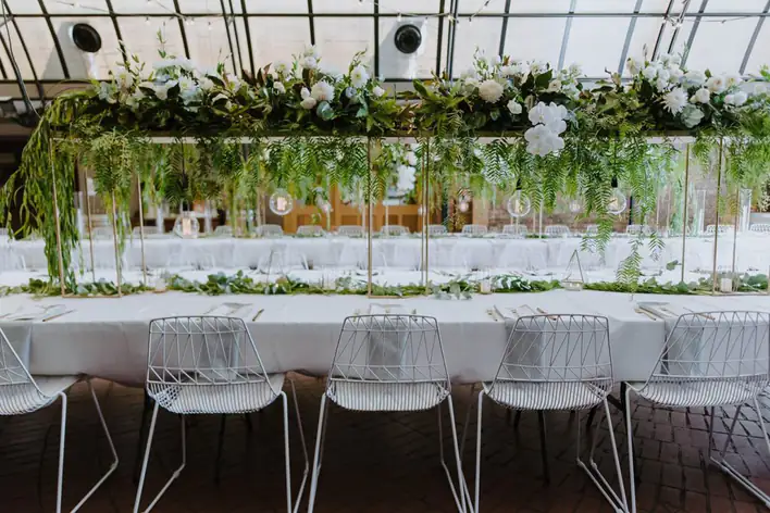 A white table with greenery and white chairs.