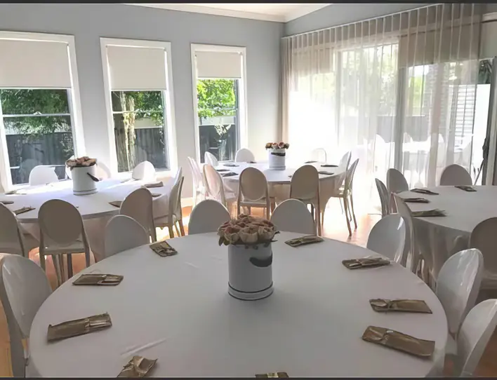 A room set up for a wedding reception with white tables and chairs.