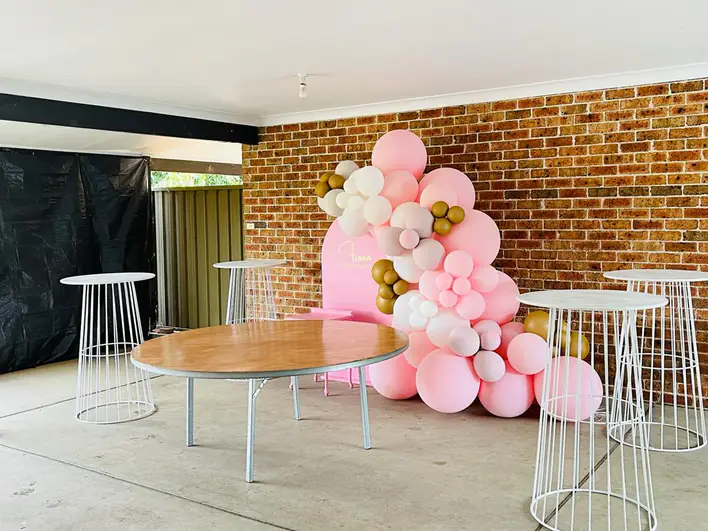 A pink and gold balloon wall in a backyard.