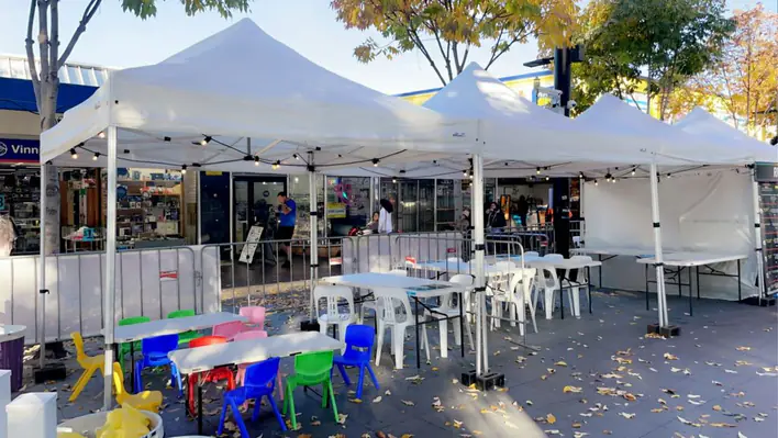 A white tent with tables and chairs on a sidewalk.