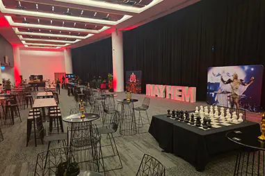 Black draping along a corporate event room with cocktail tables, lounge furniture, display signage and red accent lighting