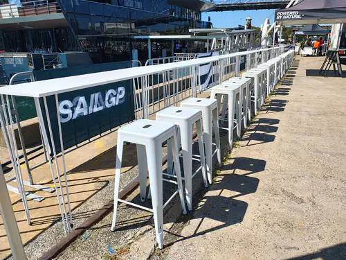 Scores of white Tolix stools set up in front of white wire tables near a boat