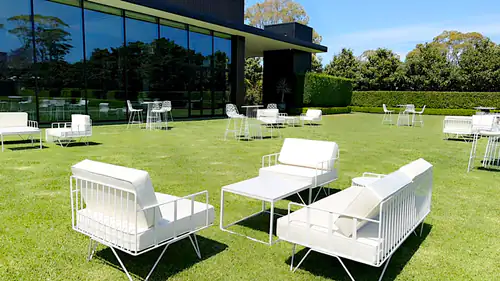 White sofa lounges and white stools with wire tables set up on a lawn in front of a business centre