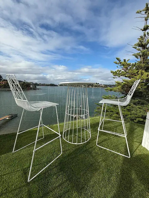 White wire table and stools hired and placed on grass in front of water