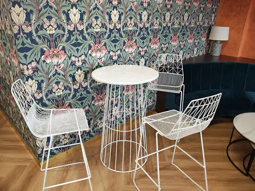 White wire table and stools in front of patterned wallpaper