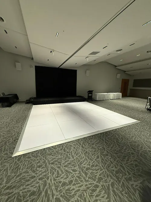 White gloss dance floor setup in a modern corporate event venue with stage platform and presentation area ready for guests