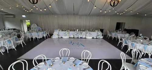 White gloss dance floor surrounded by decorated wedding reception tables and floral styling under festoon lighting