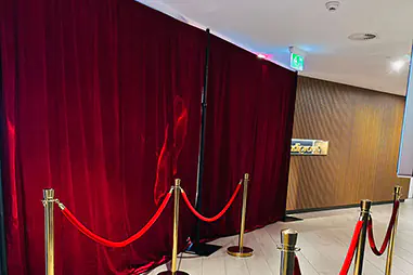 Red velvet draping with gold bollards and red ropes creating a formal event entry area inside a modern venue