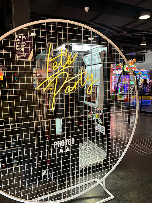 A white hoop mesh backdrop with the 'Let's Party' neon sign on it
