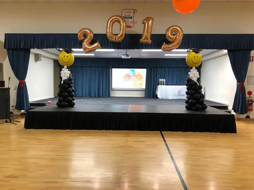 Large indoor stage platform with black skirting arranged in a spacious function room with natural light and open layout