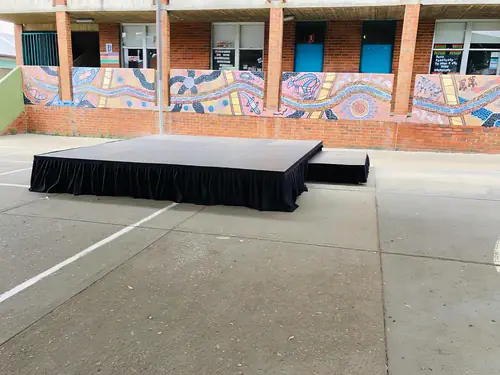 Portable stage platform with black skirting set up indoors for a presentation or event with open floor space and minimal furnishings