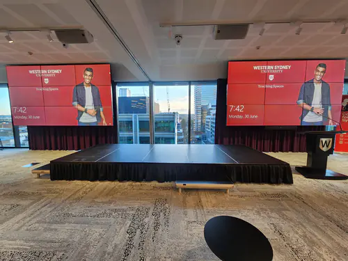 Conference stage platform positioned between large digital display screens at a university event venue