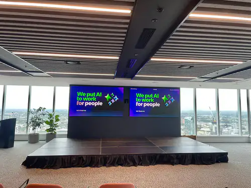 Corporate presentation stage setup with large LED display screens inside a modern conference venue overlooking the city skyline