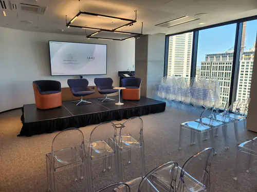 Corporate event stage with lounge chairs and small table set up for a panel discussion in a modern room overlooking city buildings