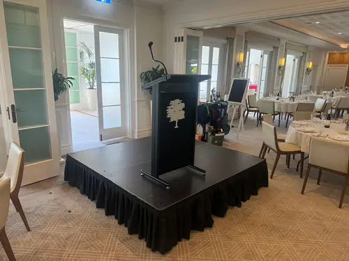 Event stage with podium positioned in a formal dining function room with round tables and place settings arranged for guests