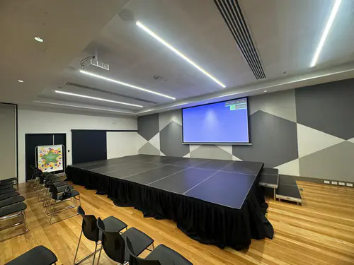Indoor modular stage platform set up in a conference room with projector screen, tiered steps, and surrounding audience seating