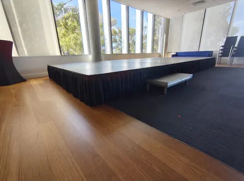 Indoor event stage platform with black skirting and access step positioned inside a modern presentation room