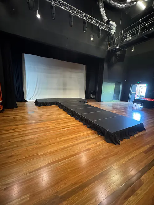 Runway-style stage platform arranged in a theatre venue with extended catwalk layout and backdrop curtain for performances or presentations