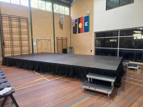 Large stage platform with access stairs positioned inside a school hall for presentations and community events