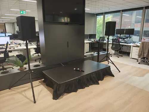 Small presentation stage with microphone and speaker setup inside a modern office environment with large display screen