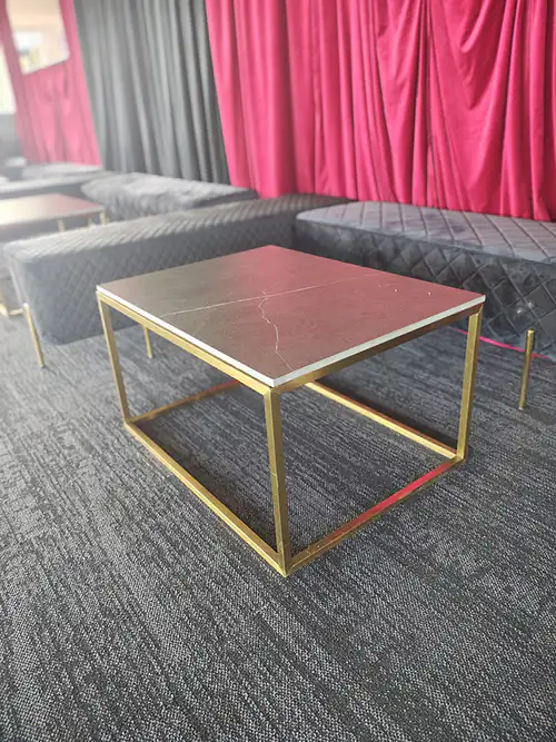 A brass-framed square coffee table in front of some red drapes