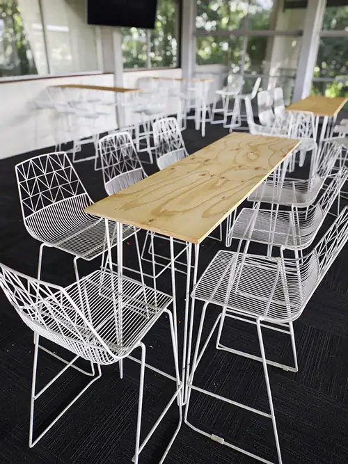 White wire stools next to some tables with timber tops