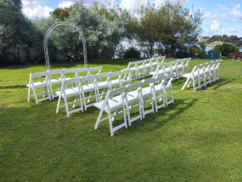 Lots of white plastic chairs set up in a park ready for a wedding