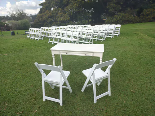 Lots of white plastic folding chairs and a signing table ready for a wedding in an outdoor park
