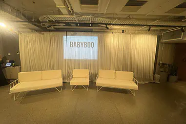 White draping behind white lounge seating, with a projected logo display and matching event furniture in an indoor venue