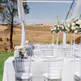 A wedding reception set up in a field with tables and white chairs hired from Clear Tiffany Chair Hire.