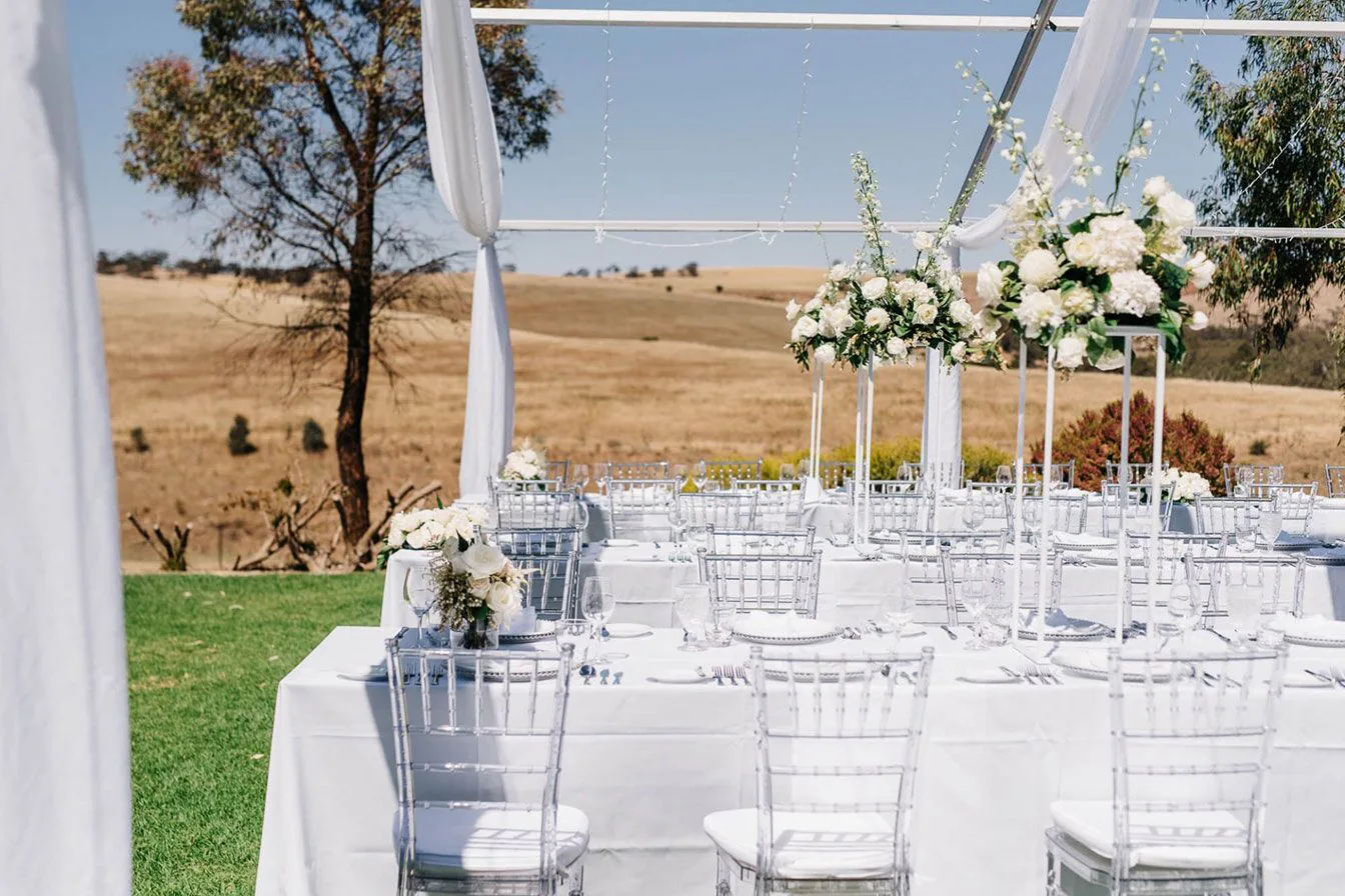 A wedding reception set up in a field with tables and white chairs hired from Clear Tiffany Chair Hire.