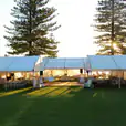 A white 8m x 21m framed marquee set up with tables and chairs on a grassy field.