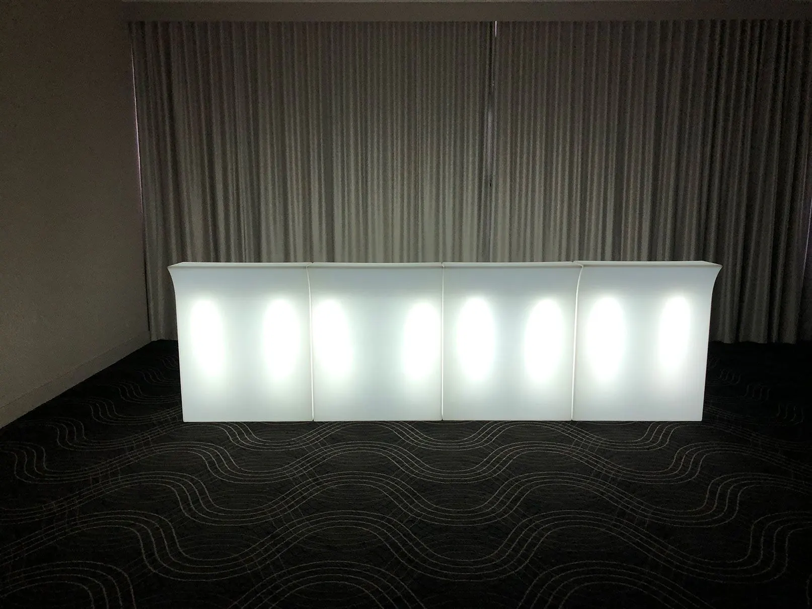 A straight white LED bar in a room with curtains, designed to glow.