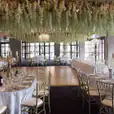 A wedding reception with white flowers hanging from the ceiling, complemented by elegant gold Tiffany chair hire.