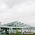 A 6m x 39m framed marquee wedding tent set up on a grassy area near the water.