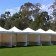 A row of white 3mx3m pop up marquees with walls on 3 sides, set up on a grassy field.