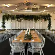 A room with tables and chairs set up for a wedding reception, featuring white arrow chair hire.