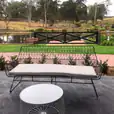 A patio with a bench and table next to a pond. The seating arrangement includes the elegant Black Arrow 3 Seater Lounge available for hire.
