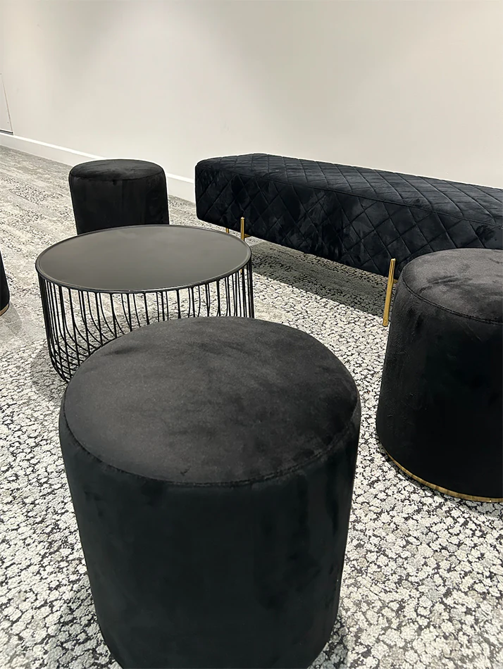 A black wire coffee table next to black ottoman stools and a lounge