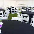 A white tent with black tables and chairs adorned with black round banquet tablecloths.