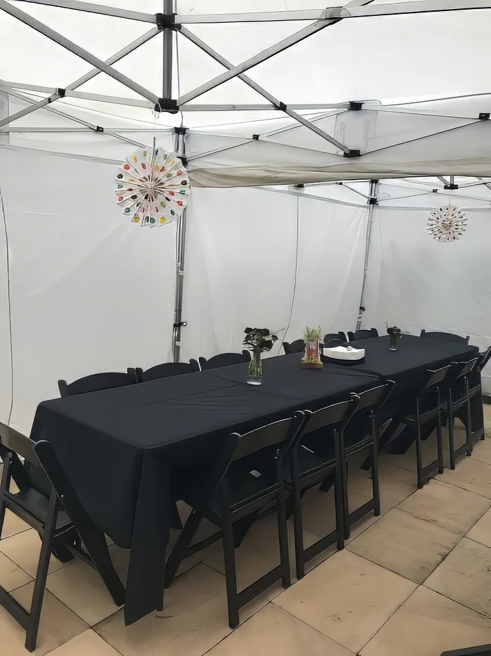 A table set up in a white tent with black chairs and a black tablecloth.