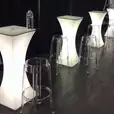Clear ghost stools placed around lighted bar tables in a room.