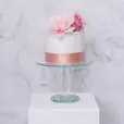 A white cake with pink flowers on a crystal cake stand.