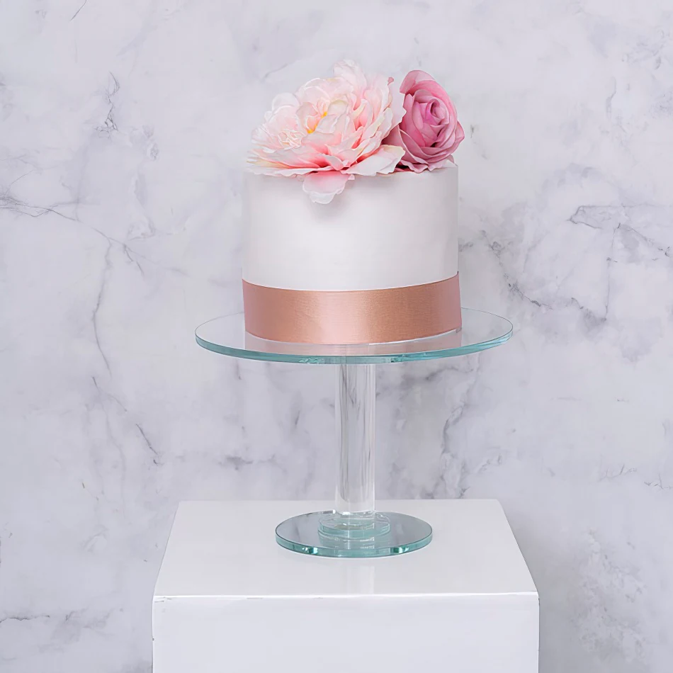 A white cake with pink flowers on a crystal cake stand.