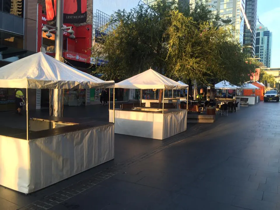 A vibrant city street adorned with numerous white tents offering fete stalls and tent hire, complete with convenient setup services.