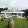 A framed marquee set up in a grassy area with wine barrels.
