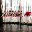 A clear acrylic table with cupcakes and red roses in front of a window.