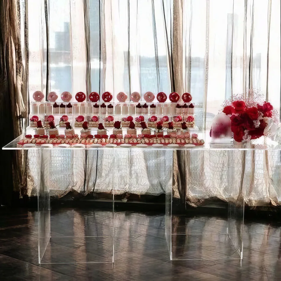 A clear acrylic table with cupcakes and red roses in front of a window.
