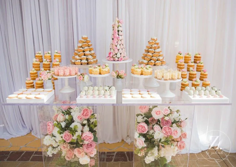 A dessert table adorned with cupcakes and flowers, featuring a Clear Acrylic Ghost Table.