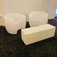 Two white chairs and a white ottoman in a room available for Glow Couch Hire.